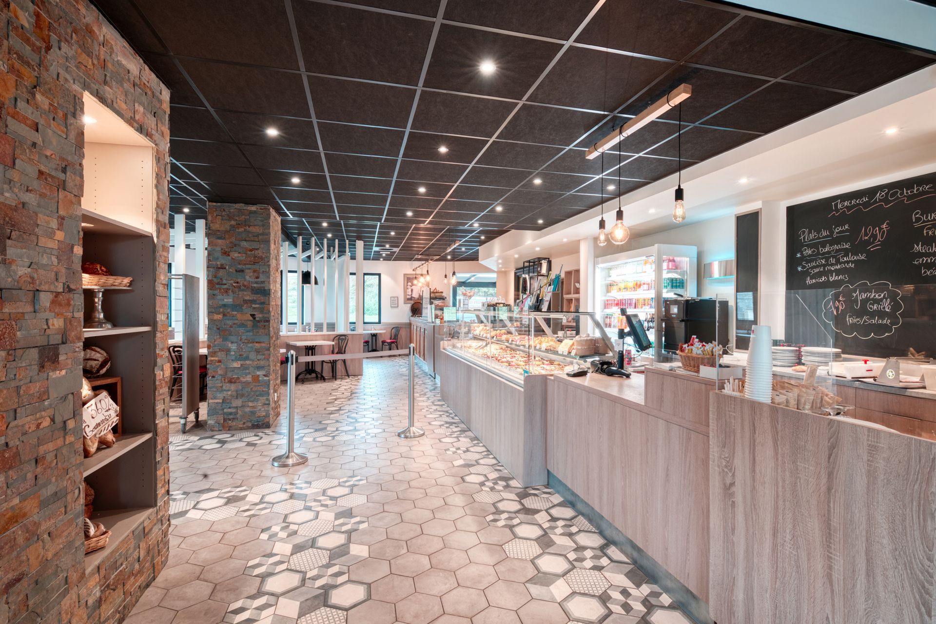 L'intérieur lumineux d'un café est orné de piliers en pierre, d'un comptoir de service en bois clair, de vitrines pour les aliments et d'un sol carrelé à motifs.