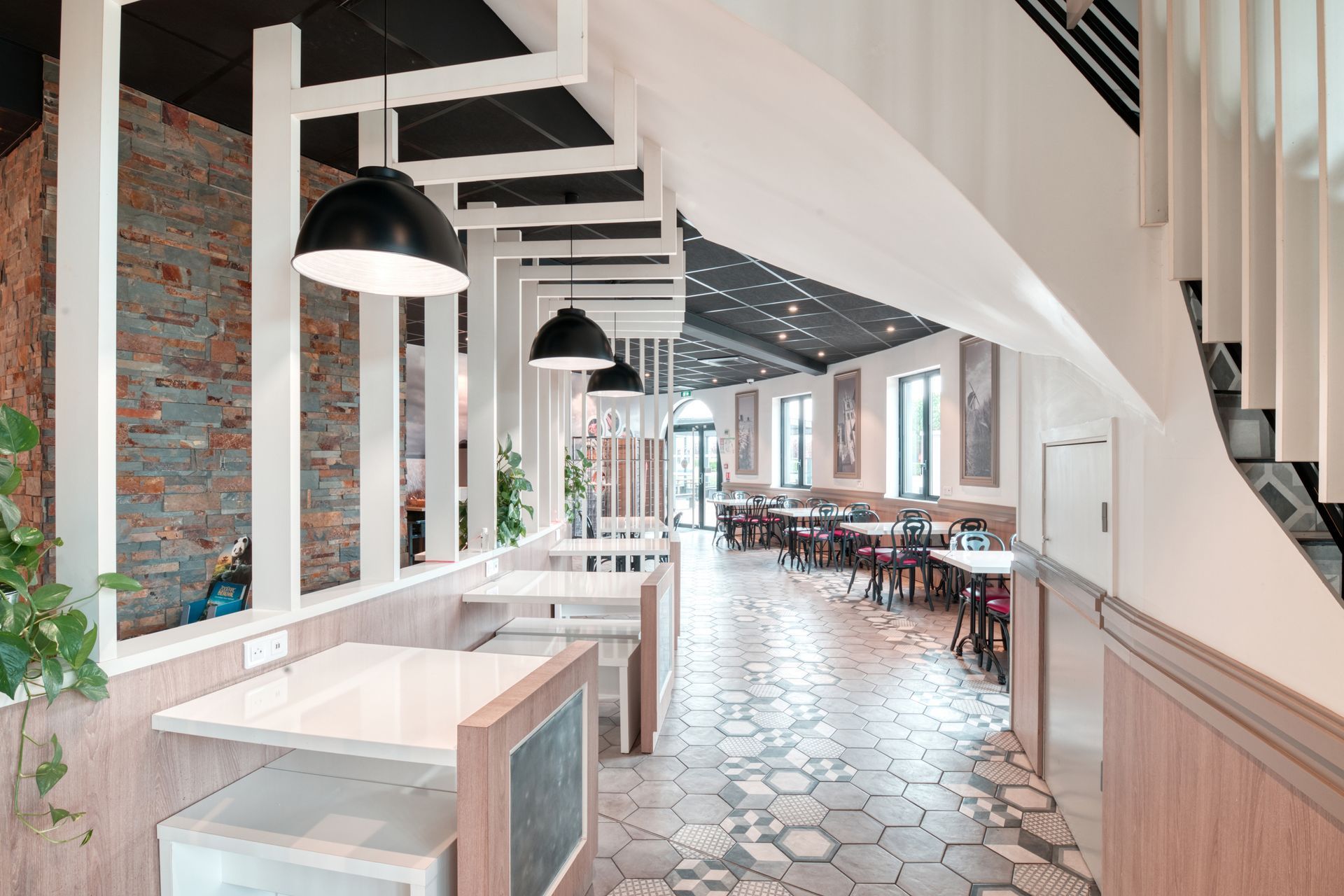Un intérieur de restaurant moderne avec des cloisons à lattes blanches, des suspensions lumineuses, des accents de briques et un sol en carreaux hexagonaux.