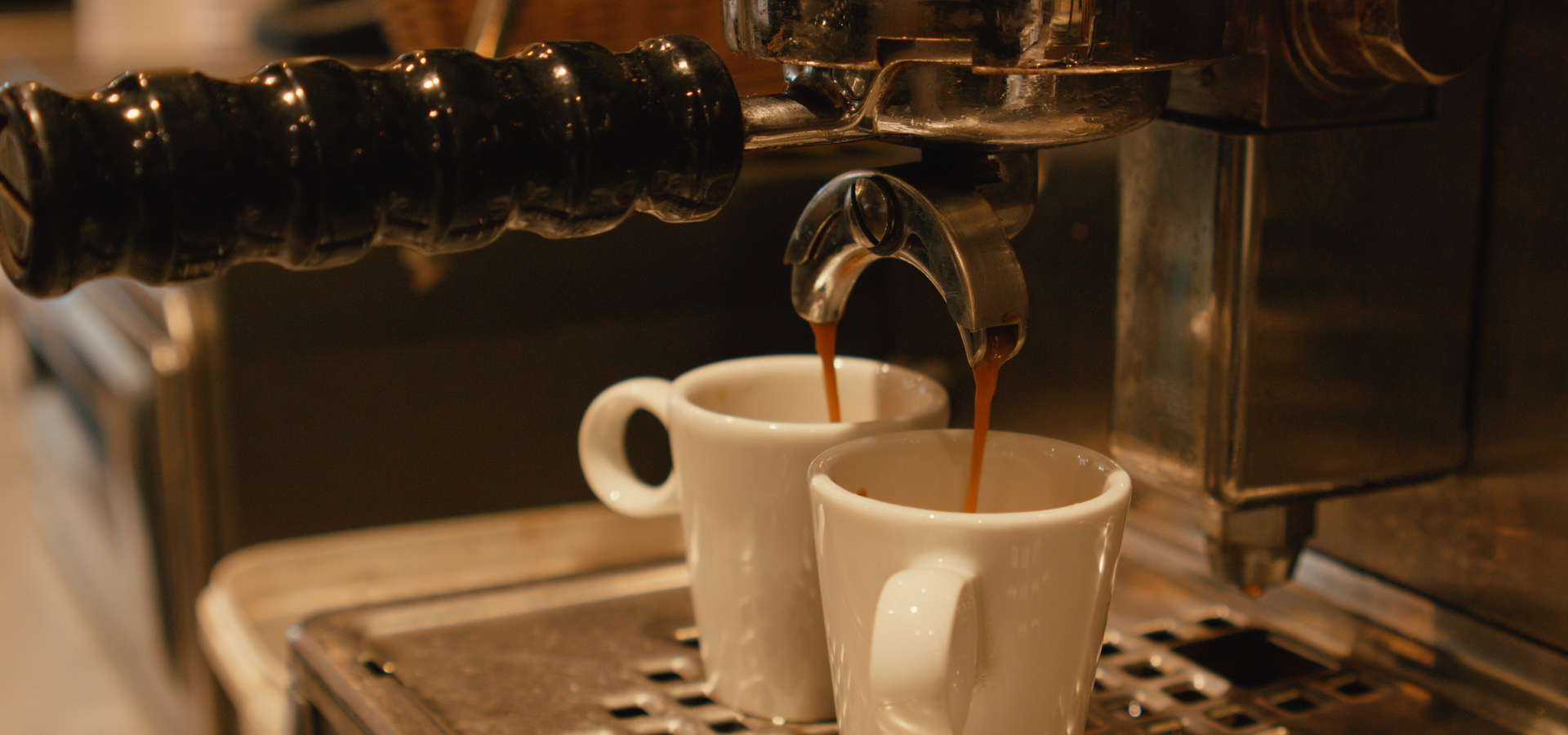 Une machine à expresso verse simultanément du café noir dans deux petites tasses en céramique blanche posées sur un plateau égouttoir en métal.