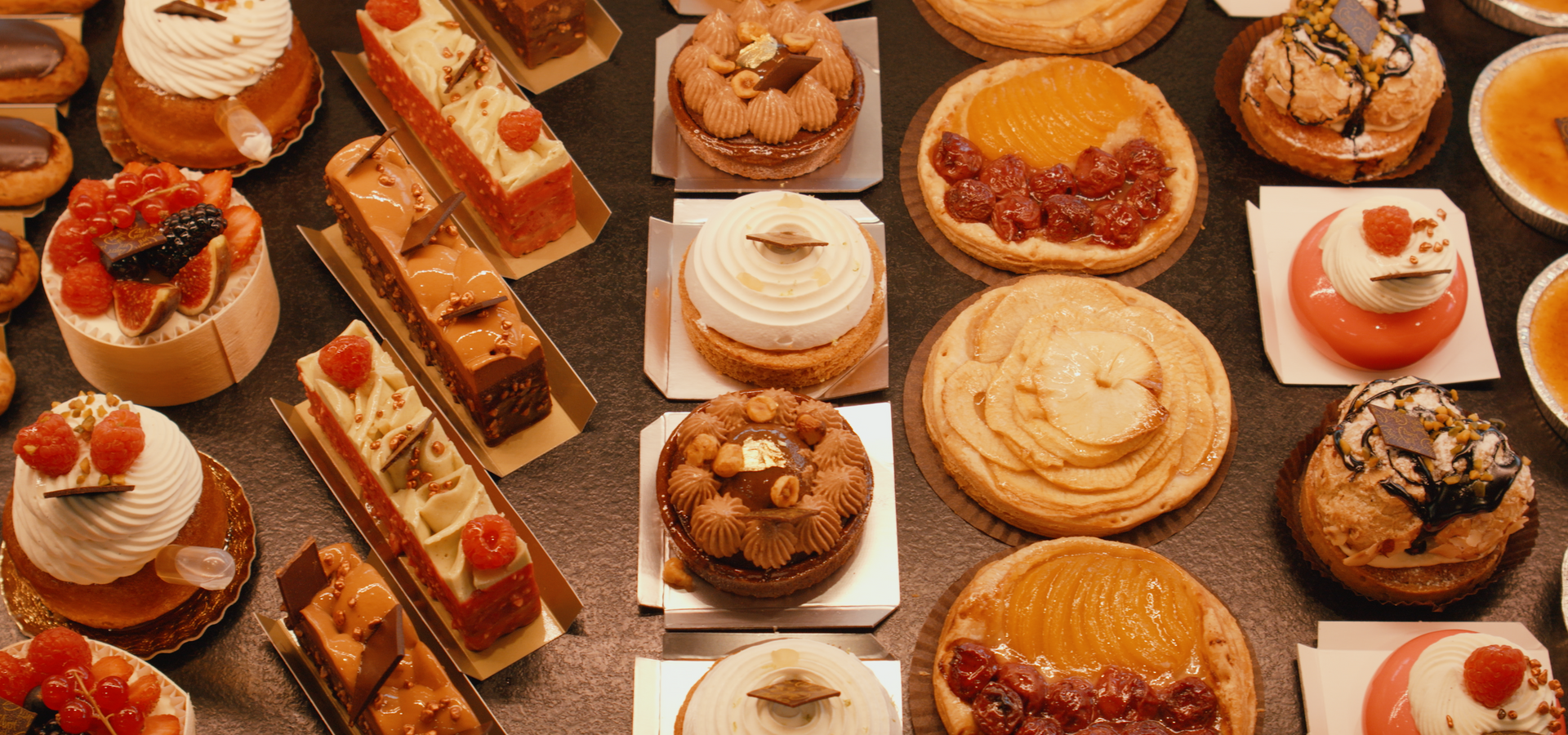 Un assortiment de pâtisseries françaises colorées et raffinées, comprenant tartes, gâteaux et éclairs, présentés dans une vitrine de boulangerie.