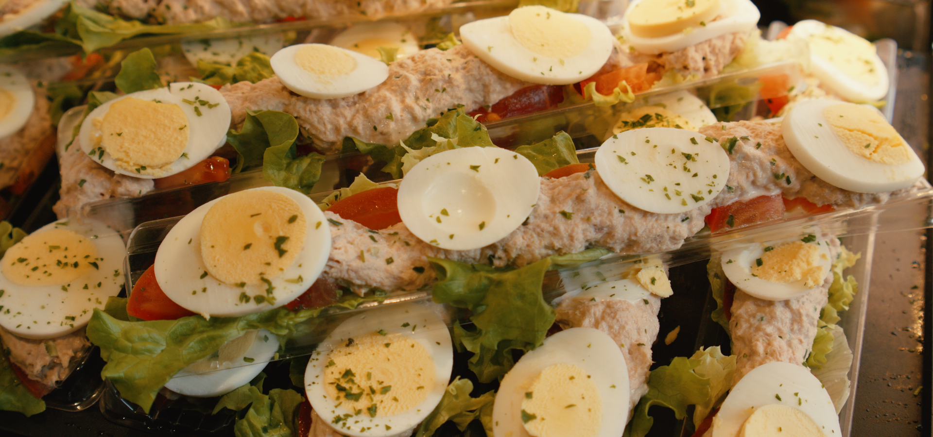 Un assortiment de tartines garnies de salade de thon, d'œufs durs tranchés, de laitue et de tomates.