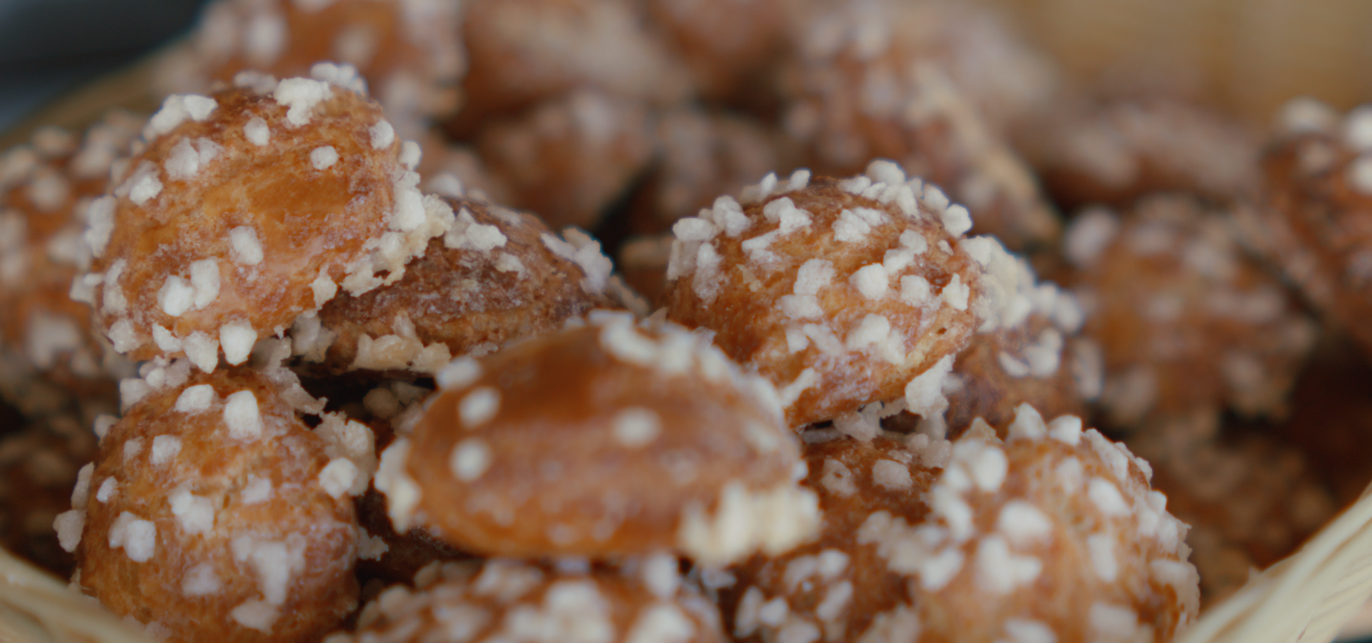 Gros plan sur de petites pâtisseries rondes et dorées, recouvertes de sucre perlé blanc à gros grains, présentées dans un panier tressé.