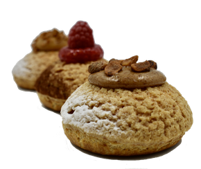 Trois choux à la crème alignés en diagonale, garnis de crème au chocolat, d'une framboise fraîche et de noix grillées, saupoudrés de sucre.