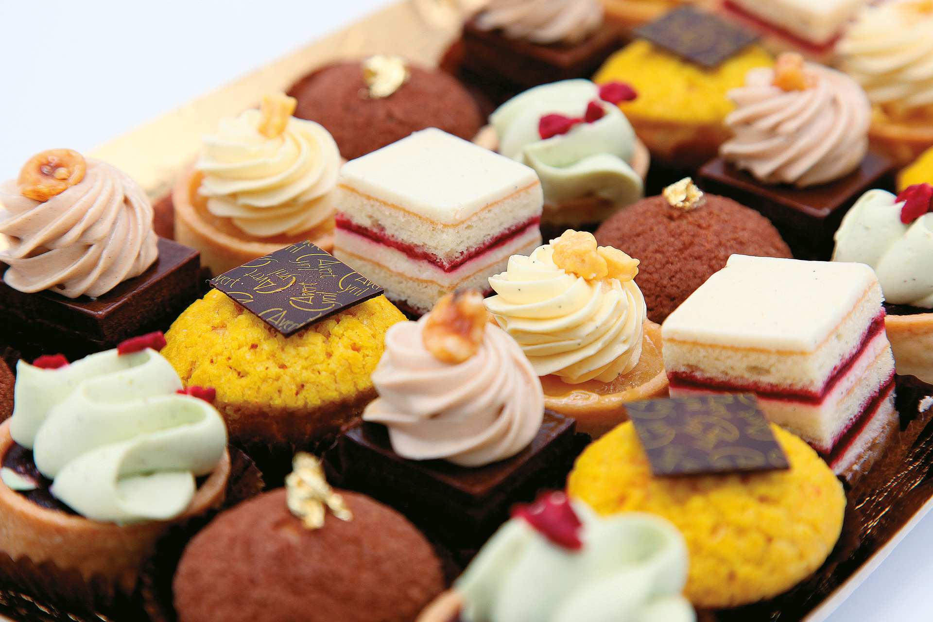 Gros plan sur un assortiment de mini-pâtisseries gourmandes, comprenant des dômes au chocolat, des tartelettes à la crème et des gâteaux à étages.