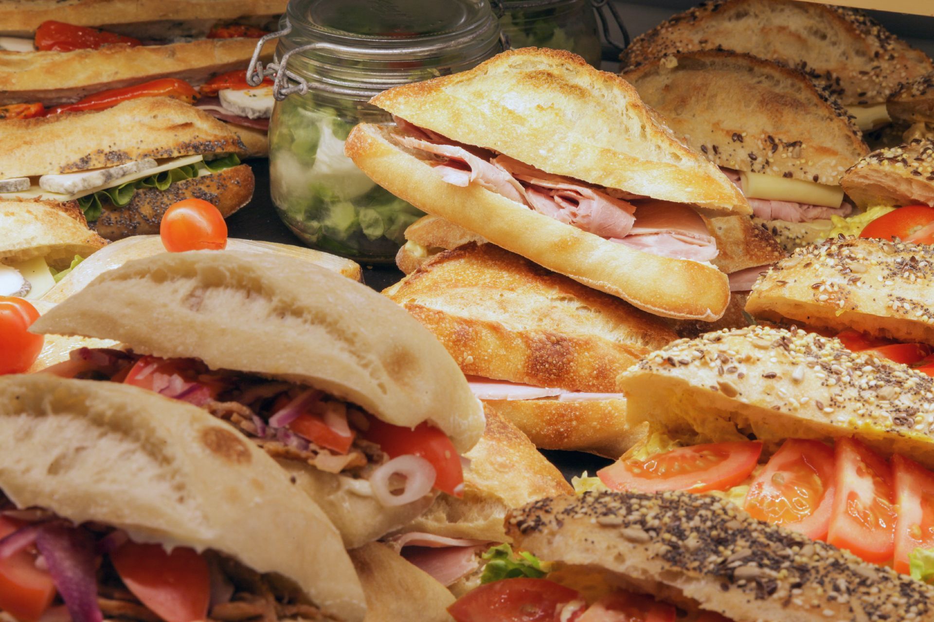 Un assortiment de sandwichs, notamment au jambon et aux légumes, est présenté sur un comptoir avec un pot de relish.