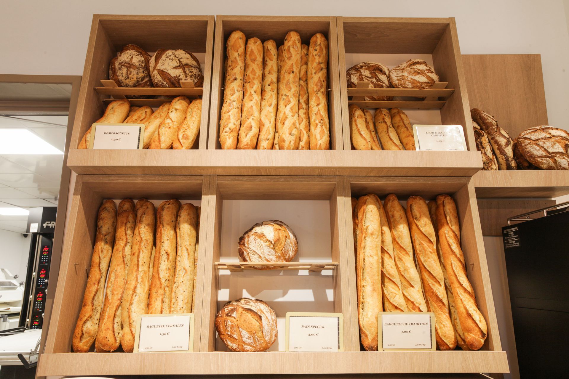 Un présentoir de boulangerie avec différents types de pain frais, notamment des rangées de baguettes et de miches rondes au levain.