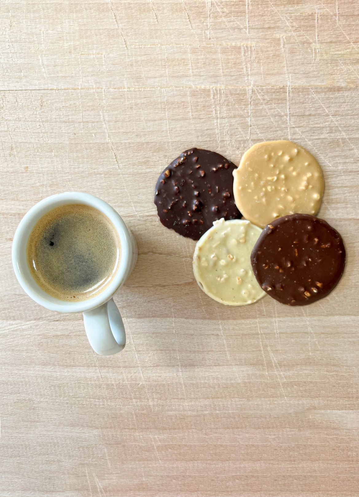 Une tasse de café et des tuiles en chocolats sur une table en bois.