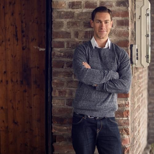 Ein Mann lehnt mit verschränkten Armen an einer Backsteinmauer