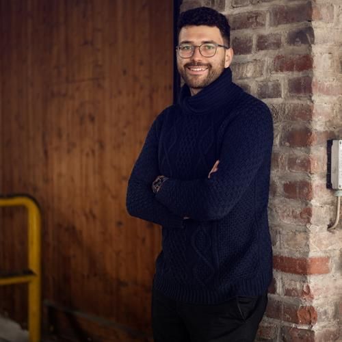 Ein Mann lehnt mit verschränkten Armen an einer Backsteinmauer