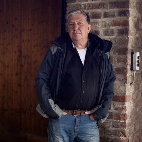 Ein Mann steht mit den Händen in den Taschen vor einer Backsteinmauer