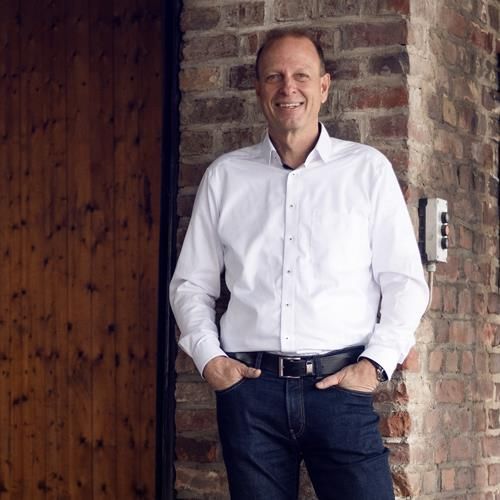 Ein Mann in einem weißen Hemd steht vor einer Backsteinmauer