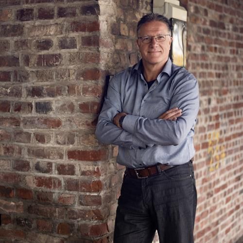 Ein Mann lehnt mit verschränkten Armen an einer Backsteinmauer