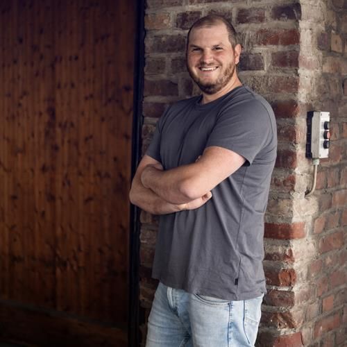 Ein Mann steht mit verschränkten Armen vor einer Backsteinmauer