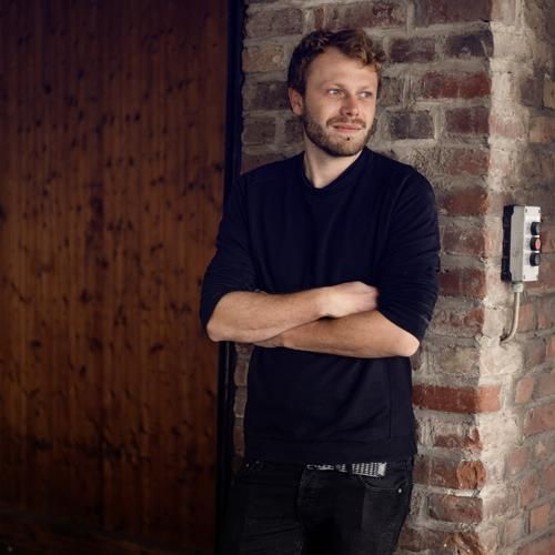 Ein Mann lehnt mit verschränkten Armen an einer Backsteinmauer