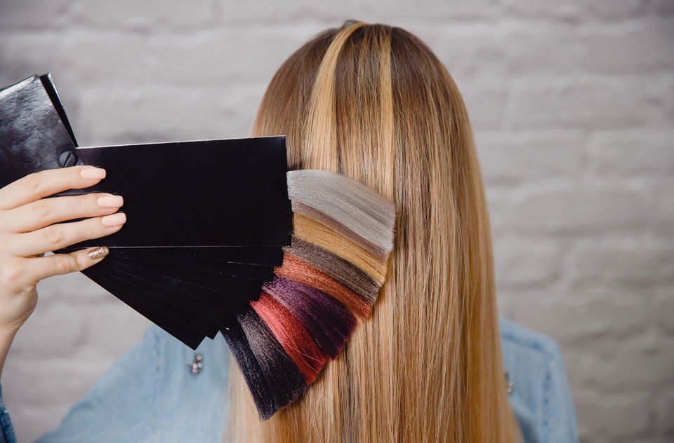 Artigiani Hairgroup – Jemand hält verschiedene Haarfarben an das blonde Haar einer Frau