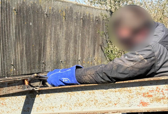 Une personne soude une structure métallique à l'extérieur, portant des gants bleus.