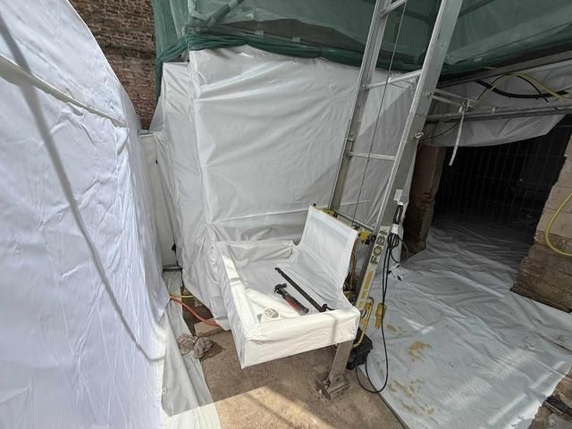 Chantier de construction avec bâches en plastique blanc, un élévateur avec siège et des outils.