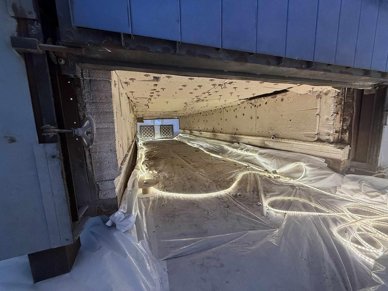 Vue intérieure d'un espace en forme de tunnel. Le sol est recouvert d'une bâche en plastique blanc. Le tunnel est blanc et rectangulaire, avec une fenêtre à son extrémité.