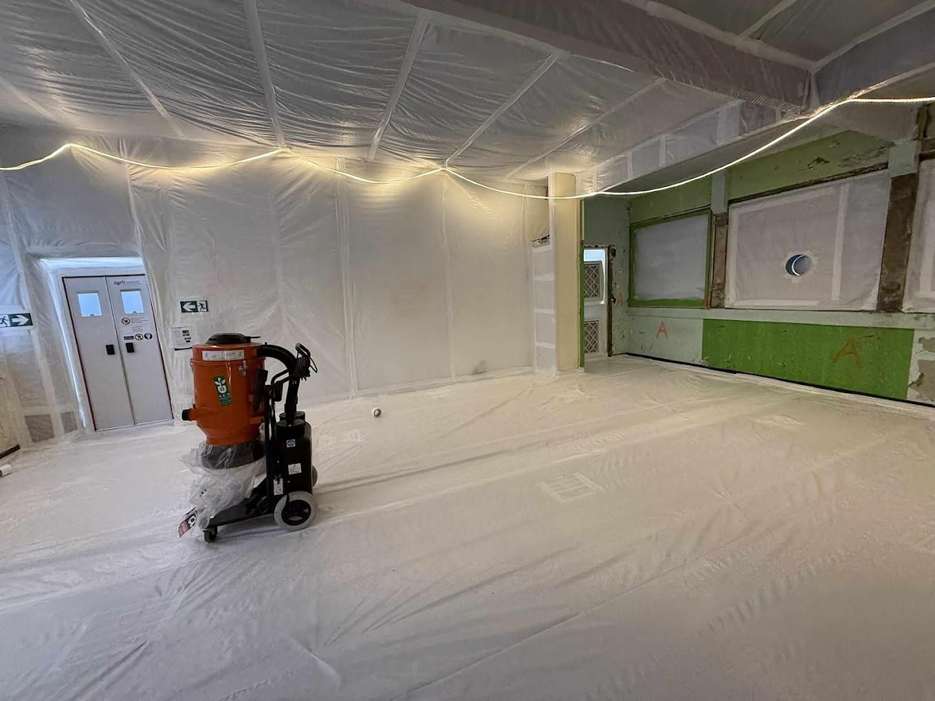 Pièce en travaux, recouverte de bâches en plastique blanc, avec un aspirateur et des guirlandes lumineuses.