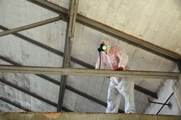 Une personne en combinaison de protection inspecte le plafond d'un bâtiment.