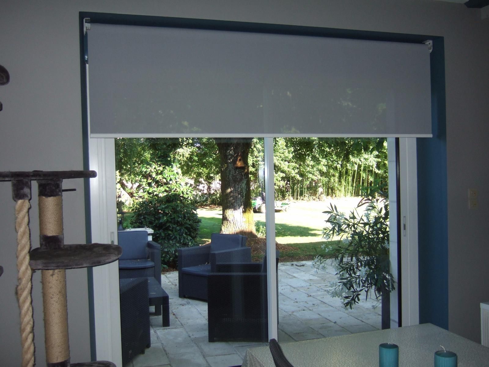 Un store enrouleur recouvre partiellement une porte vitrée donnant sur une terrasse extérieure.