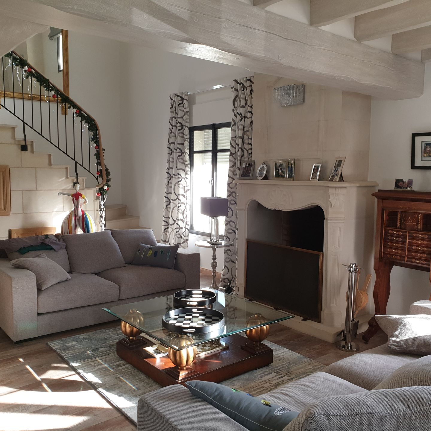 Salon avec canapé, cheminée, escalier et table basse en verre.