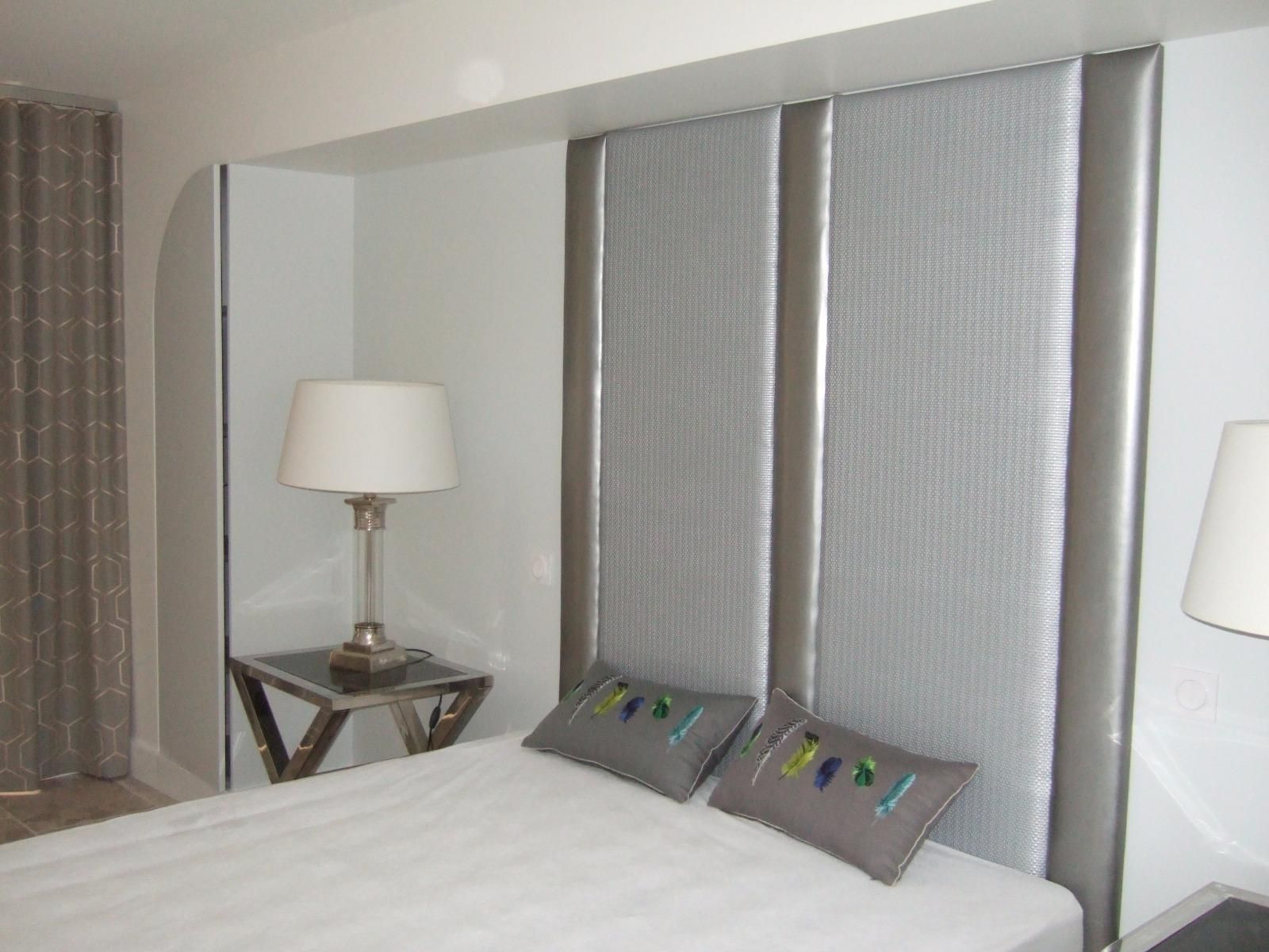 Tête de lit rembourrée, table de chevet avec lampe et coussins décoratifs.