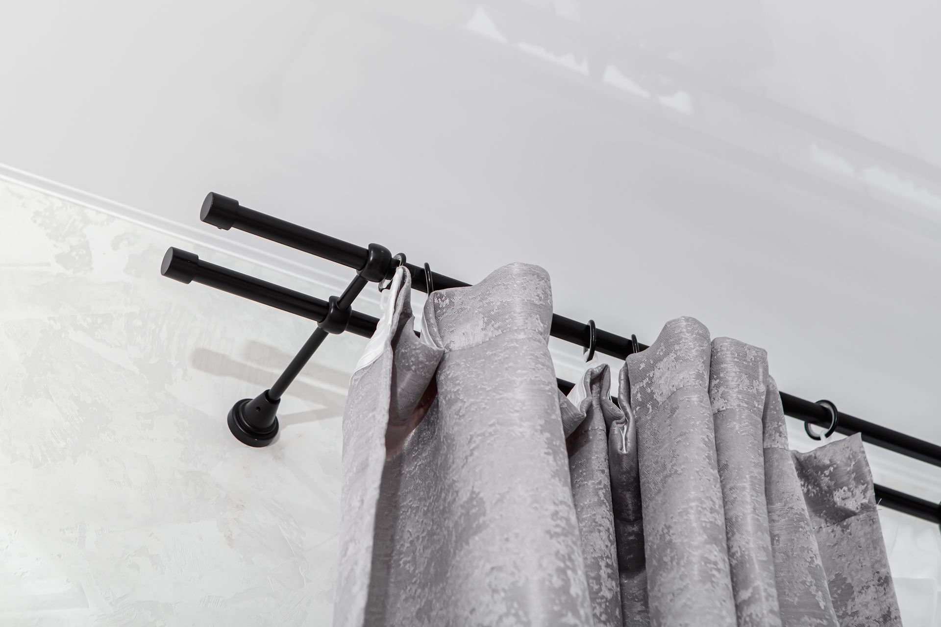 Tringle à rideaux noire avec rideaux gris à motifs sur un mur et un plafond blancs.