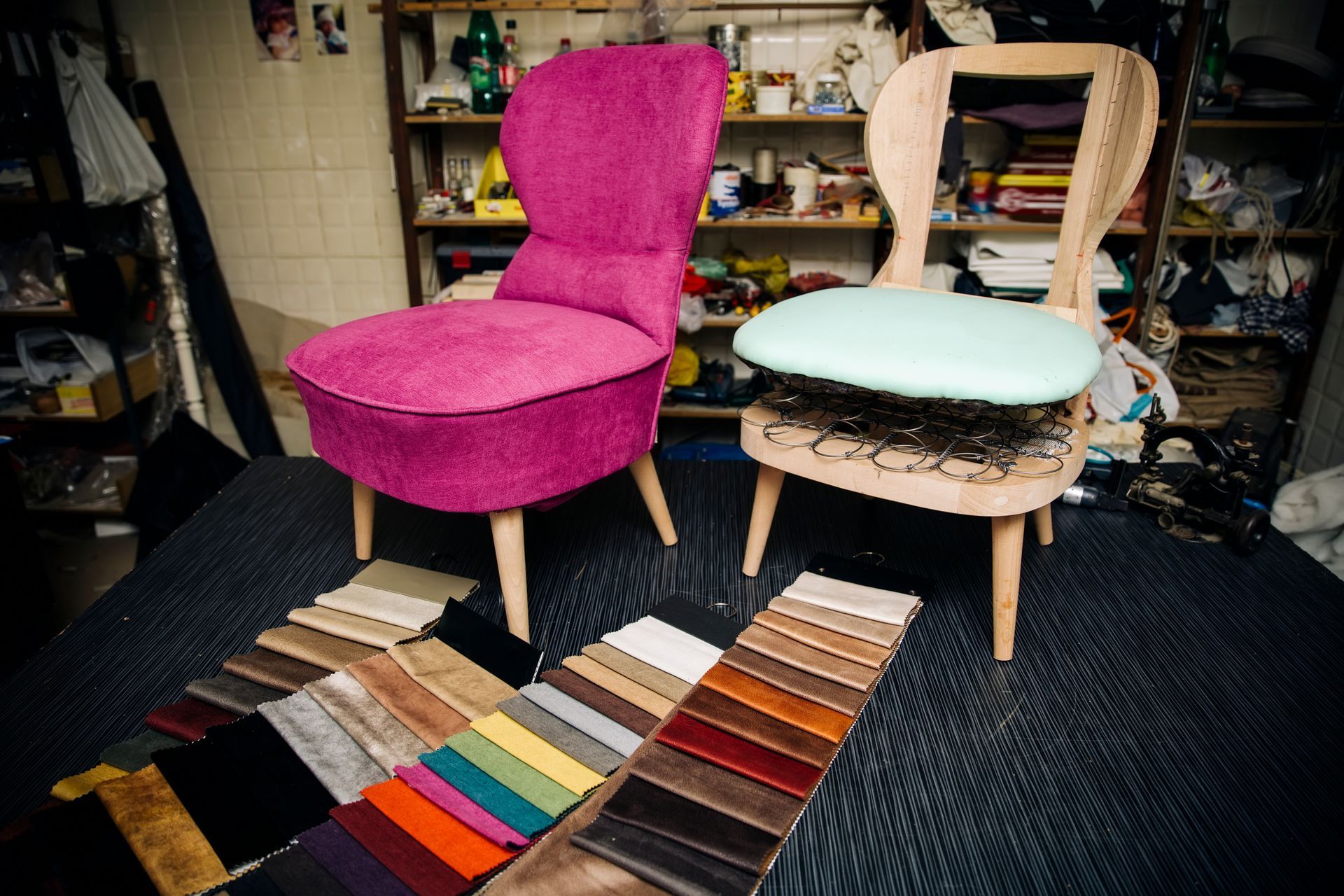 Une chaise magenta finie à côté d'une chaise en cours de rembourrage avec des échantillons de tissu sur une table.
