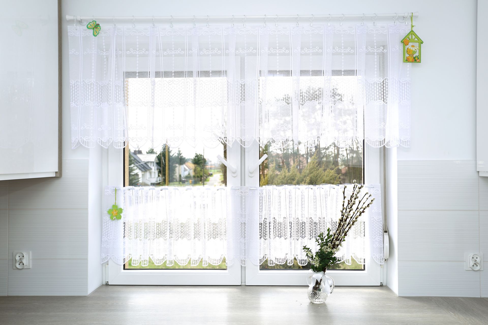Des rideaux de dentelle blanche encadrent une fenêtre donnant sur une cour.