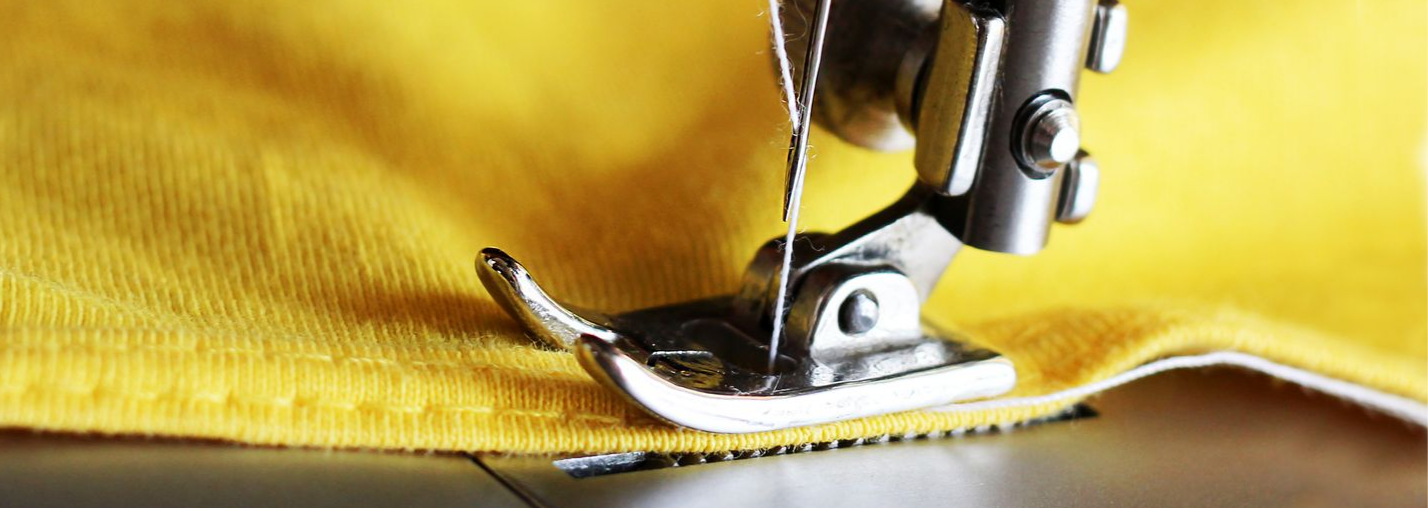Une aiguille de machine à coudre qui perce un tissu jaune.