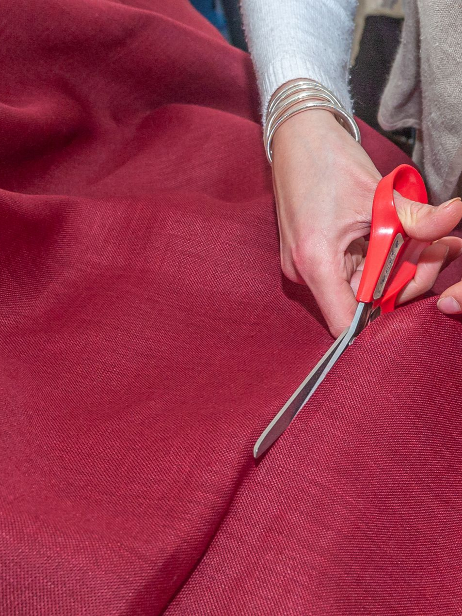 Des mains tenant des ciseaux découpent un grand morceau de tissu rouge.