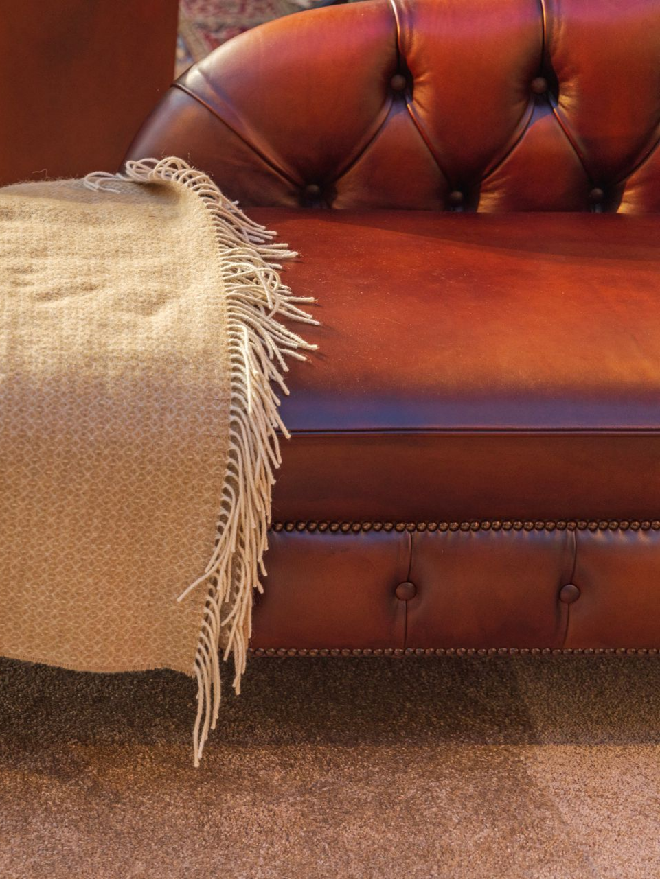 Canapé en cuir marron avec un plaid beige.