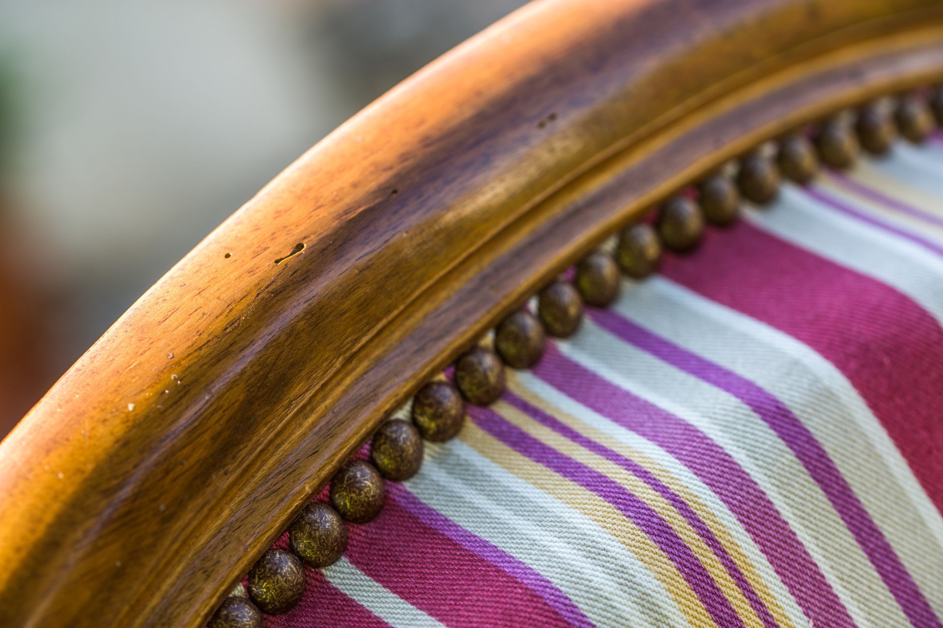 Gros plan sur le dossier d'une chaise ornée de clous décoratifs et recouverte d'un tissu rayé.