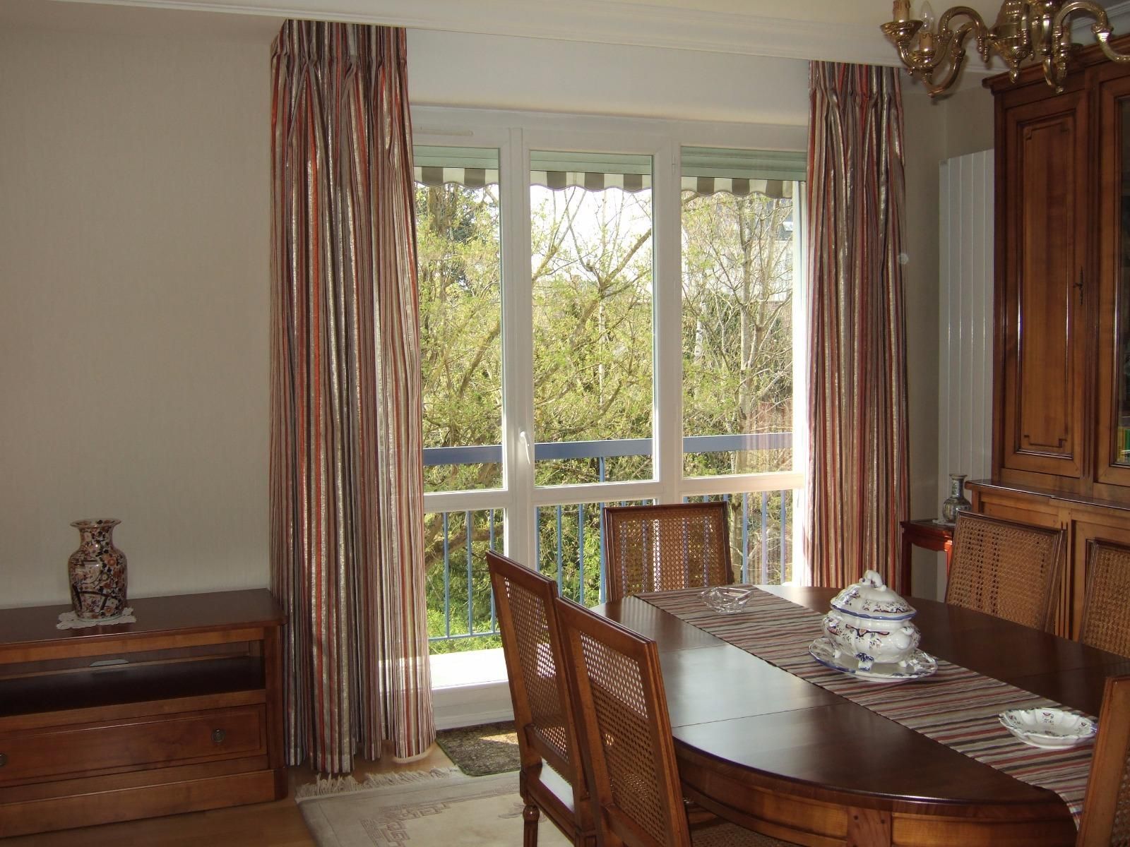 Salle à manger avec table, chaises, fenêtre avec rideaux à rayures et meubles en bois.