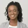 A woman with dreadlocks is smiling and wearing a grey jacket.