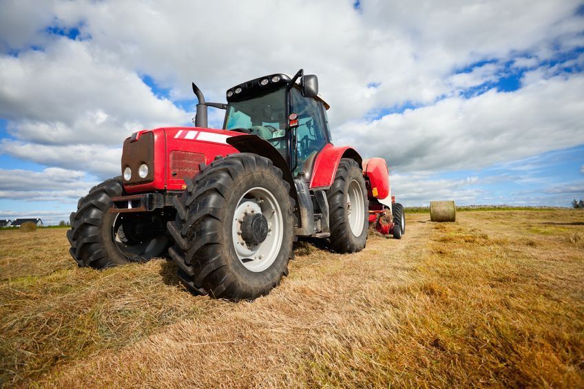 Un tractor rojo está empacando heno en un campo.