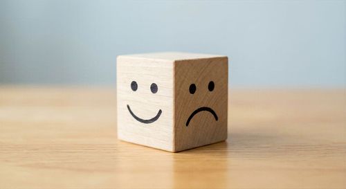 Petit bloc de bois avec un visage souriant d'un côté et un visage triste de l'autre, posé sur une table.