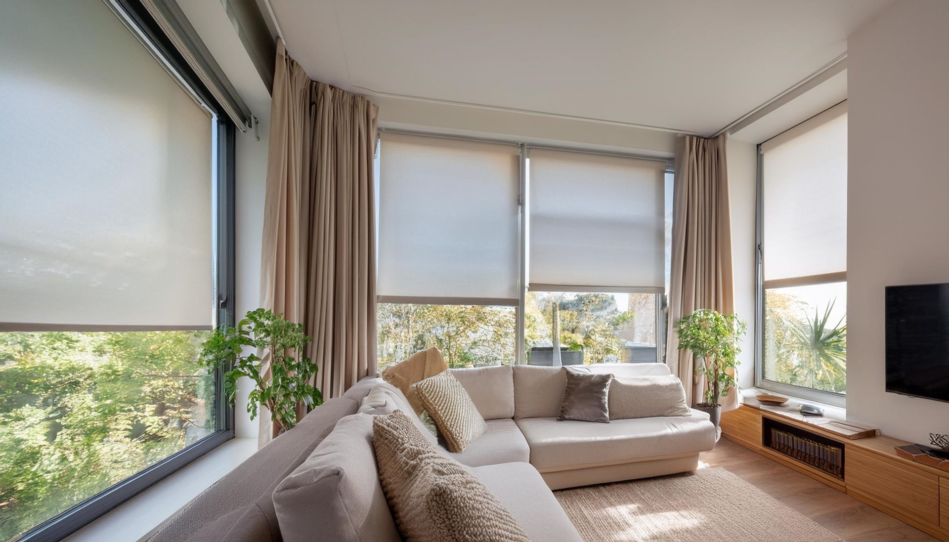 Salon lumineux avec de grandes fenêtres, un canapé beige et une plante en pot donnant sur les arbres