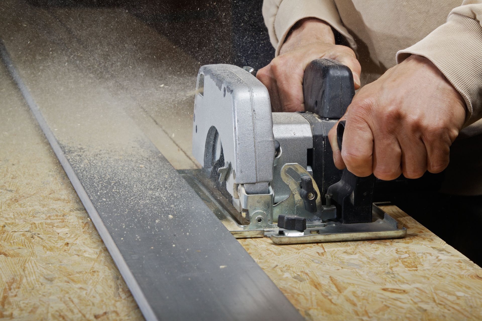 Des mains utilisent une scie circulaire pour couper une planche sur un établi.