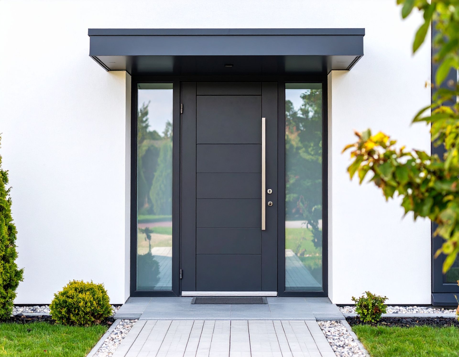 Porte d'entrée moderne avec panneaux de verre foncé et petit auvent, intégrée à un mur extérieur blanc.