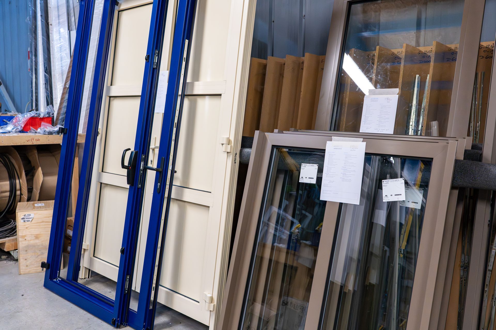Présentation en atelier de cadres de fenêtres et de panneaux de verre empilés contre un mur