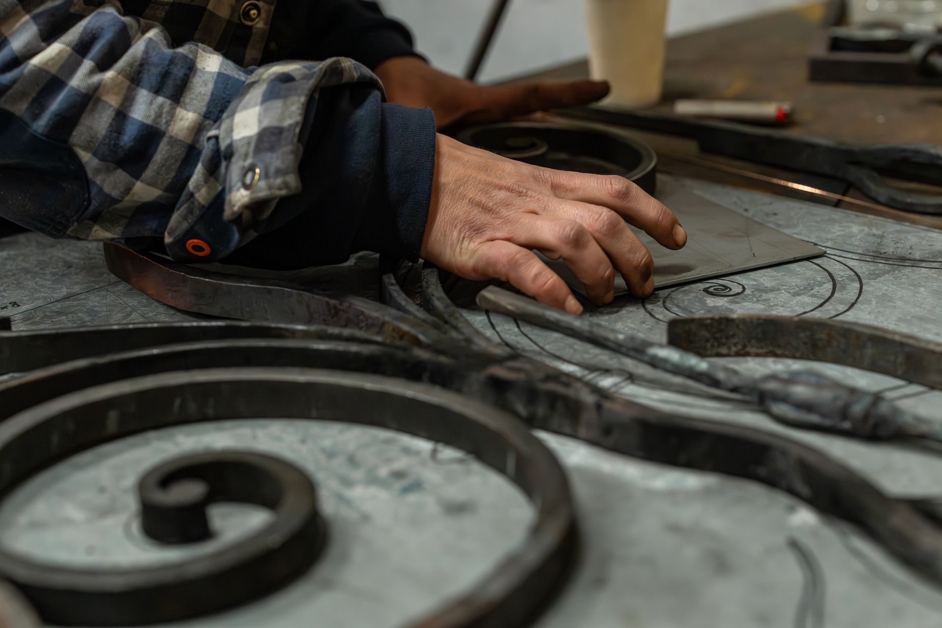 Des mains façonnent une pièce de métal en volutes sur un établi dans un atelier de métallurgie.
