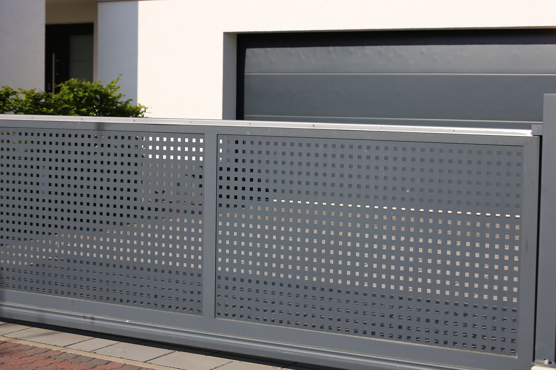 Portail d'allée en métal perforé gris devant une maison et un garage modernes