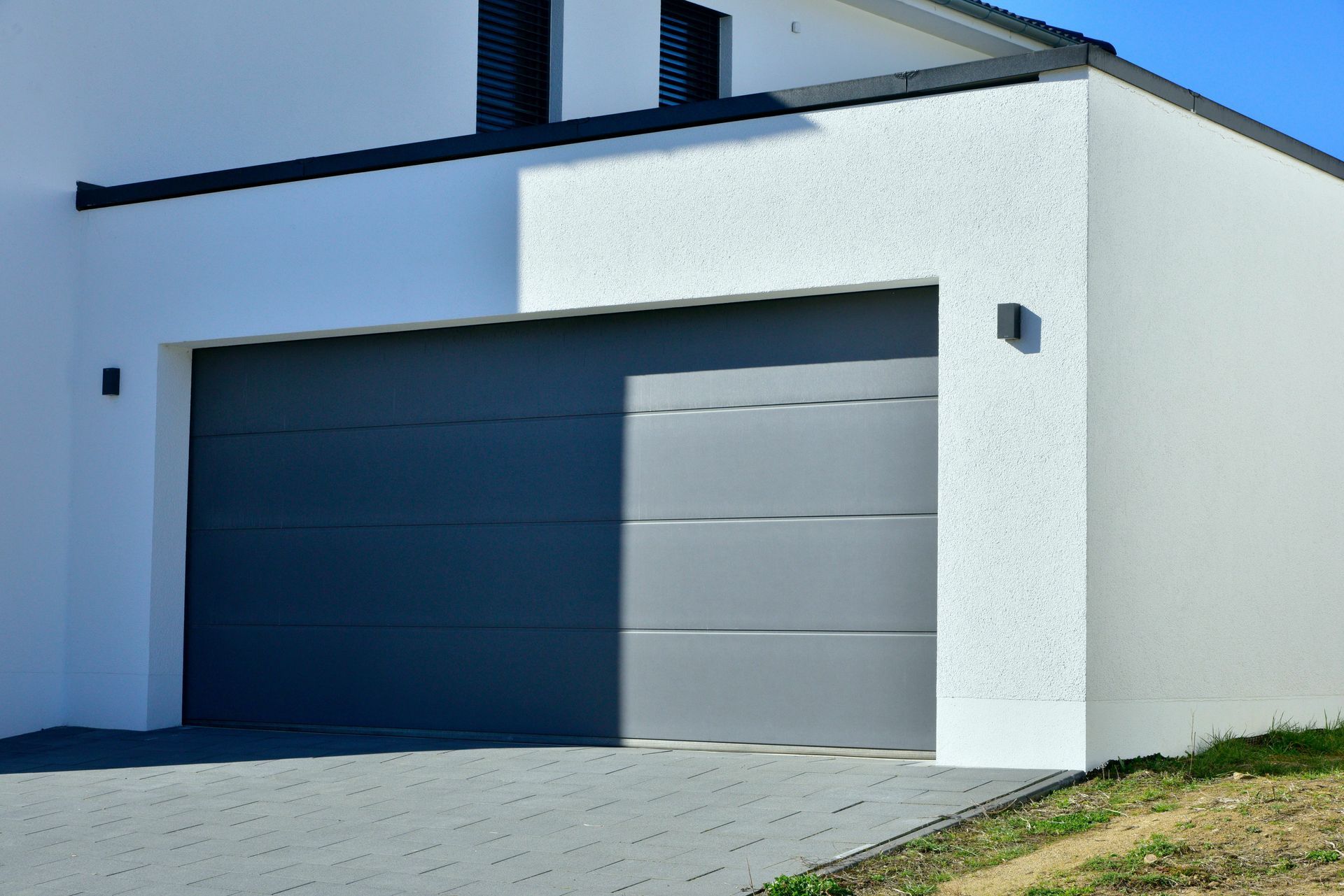 Maison blanche moderne avec porte de garage grise baignée de soleil