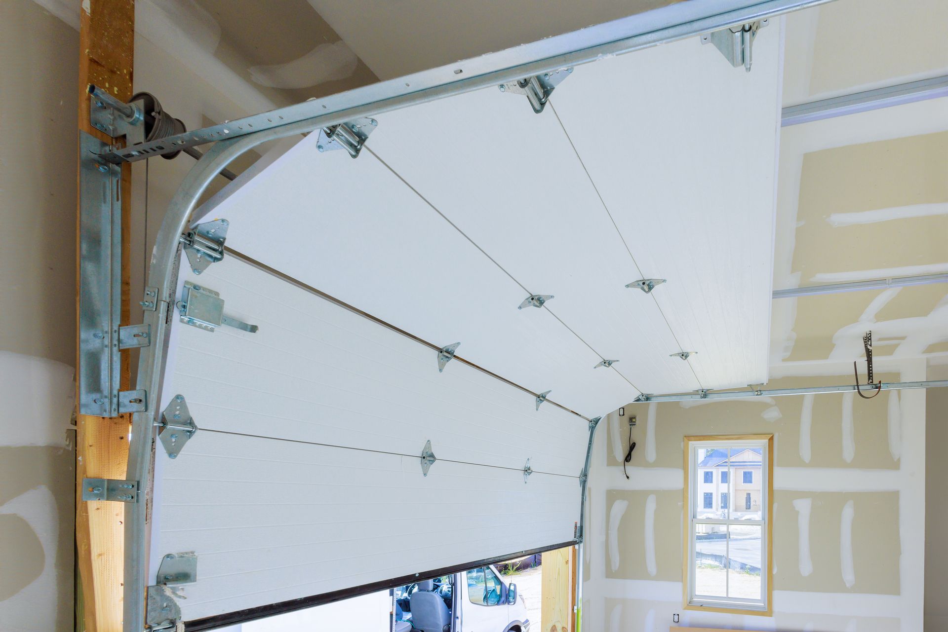 Porte de garage sectionnelle blanche partiellement installée avec rails métalliques dans une pièce non finie