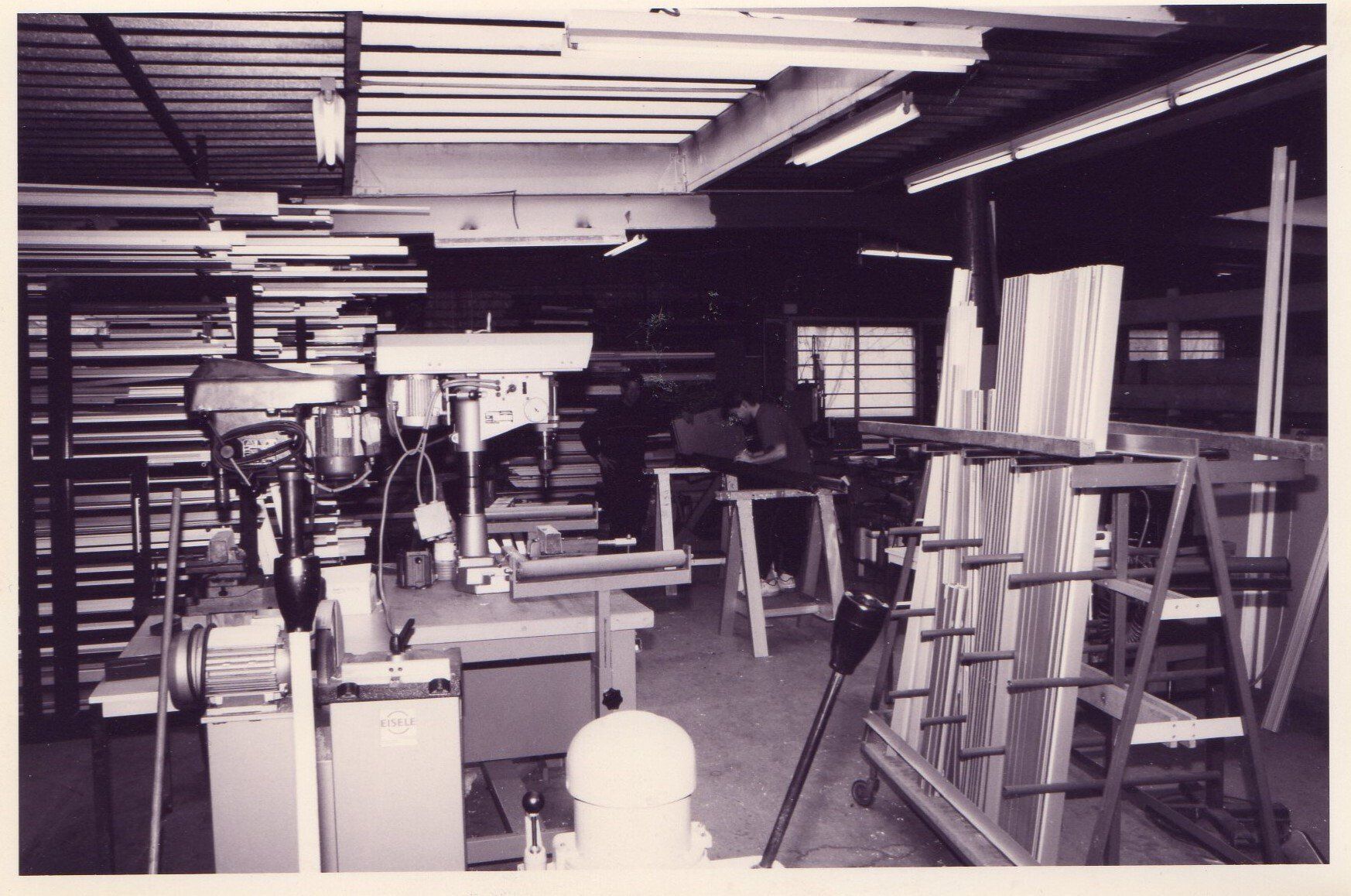 Atelier en noir et blanc avec outils, établis, bois de construction et une échelle dans un espace encombré ressemblant à un garage