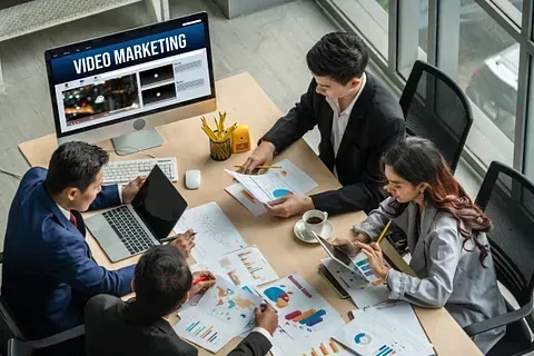 Equipo empresarial colaborando alrededor de una mesa, analizando datos de marketing, con un monitor que muestra 