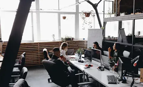 Oficina con gente trabajando en escritorios; un interior luminoso y moderno con grandes ventanas.