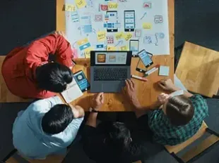 Cuatro personas alrededor de una mesa con diseños de aplicaciones móviles, intercambiando ideas.